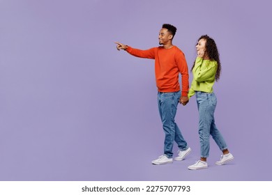 Full body side view young couple two friend family man woman of African American ethnicity wear casual clothes hold hands walk go together point finger aside isolated on pastel plain purple background - Shutterstock ID 2275707793