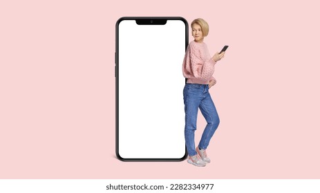 Full body side view young woman wear pink casual sweater lean on blank isolated PNG screen mobile cell phone with area use smartphone isolated on plain pastel light background.