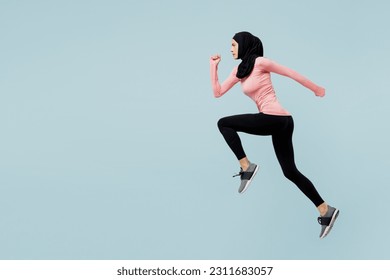 Full body side view young asian muslim fitness trainer sporty woman wear pink abaya hijab spend time in gym run fast jump high isolated on plain blue background studio. Workout sport fit abs concept - Powered by Shutterstock