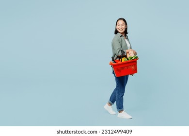 Full body side view young woman wear casual clothes hold red basket with food products look aside on area isolated on plain blue background studio portrait. Delivery service from shop or restaurant - Powered by Shutterstock