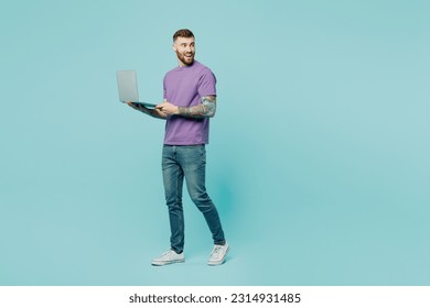 Full body side view young IT man he wears purple t-shirt hold use work on laptop pc computer look aside on area isolated on plain pastel light blue cyan background studio portrait. Lifestyle concept - Powered by Shutterstock