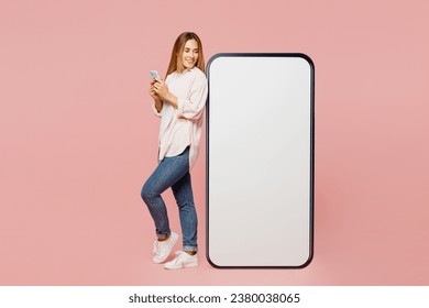 Full body side view young woman she wearing shirt white t-shirt casual clothes look at big huge blank screen mobile cell phone with area use smartphone isolated on plain pastel light pink background - Shutterstock ID 2380038065