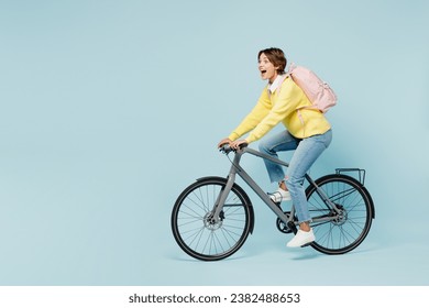 Full body side view young shocked surprised woman student wears casual clothes sweater backpack bag ride bicycle look aside isolated on plain blue background. High school university college concept - Powered by Shutterstock