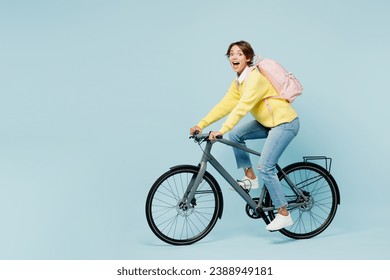 Full body side view young shocked surprised woman student wears casual clothes sweater backpack bag ride bicycle look camera isolated on plain blue background. High school university college concept - Powered by Shutterstock