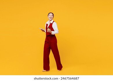 Full body side view young lawyer employee business woman of Asian ethnicity wear formal red vest shirt work at office hold use mobile cell phone drink coffee isolated on plain yellow background studio - Powered by Shutterstock