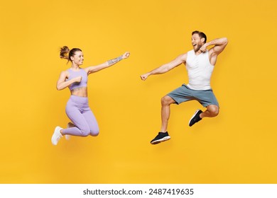 Full body side view young strong fitness trainer sporty two man woman wear blue clothes spend time in home gym jump high hop pov fight isolated on plain yellow background. Workout sport fit concept - Powered by Shutterstock