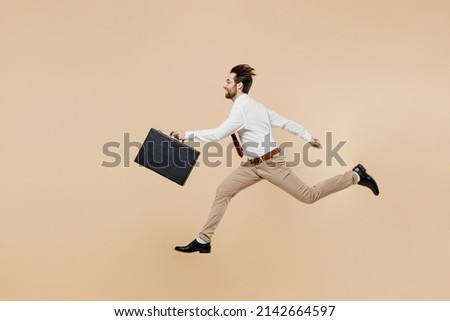 Full body side view young employee business man corporate lawyer 20s wear white shirt red tie glasses work in office jump run fast hold briefcase isolated on plain beige background studio portrait.