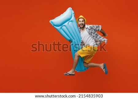 Full body side view young happy tourist man wear beach shirt hat hold inflatable mattress jump high run isolated on plain orange background studio portrait. Summer vacation sea rest sun tan concept