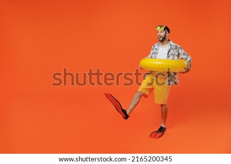 Full body side view young tourist man in beach shirt goggles hold inflatable ring flippers travel abroad on weekends isolated on plain orange background studio Summer vacation sea rest sun tan concept