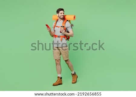 Full body side view young traveler white man carry backpack stuff mat walk use mobile cell phone isolated on plain green background. Tourist leads active lifestyle Hiking trek rest travel trip concept