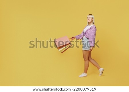 Full body side view young blonde woman 20s wear pink tied shirt white t-shirt holding package bags with purchases after shopping walk go isolated on plain yellow background People lifestyle concept