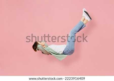 Full body side view young happy woman 20s she wear green shirt white t-shirt fly up hover over air fall down isolated on plain pastel light pink background studio portrait. People lifestyle concept