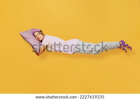 Full body side view young woman she wears purple pyjamas jam sleep eye mask rest relax at home fly fall hover over head on pillow isolated on plain yellow background studio portrait. Night nap concept
