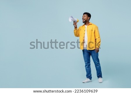 Full body side view young man of African American ethnicity 20s he wearing yellow shirt hold scream in megaphone announces discounts sale Hurry up isolated on plain pastel light blue background studio
