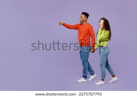 Full body side view young couple two friend family man woman of African American ethnicity wear casual clothes hold hands walk go together point finger aside isolated on pastel plain purple background