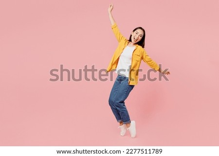 Full body side view young woman of Asian ethnicity wears yellow shirt white t-shirt leaning back with outstretched hands stand on toes isolated on plain pastel light pink background studio portrait