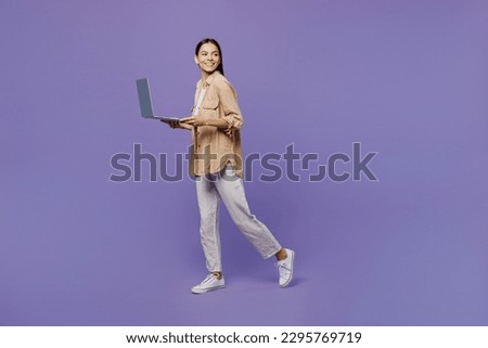 Full body side view young IT latin woman wear light shirt casual clothes hold use work on laptop pc computer look aside on area go isolated on plain pastel purple color background. Lifestyle concept