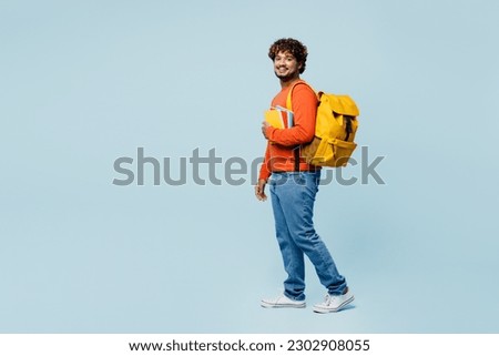 Full body side view young teen Indian boy student he wearing casual clothes backpack bag hold books walk go isolated on plain pastel light blue cyan background. High school university college concept