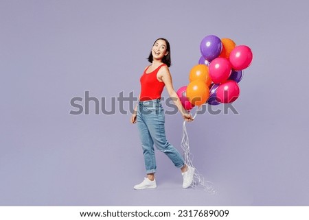 Full body side view young woman of Asian ethnicity she wear casual clothes red tank shirt hold bunch of colorful air balloons isolated on plain pastel light purple background studio. Lifestyle concept