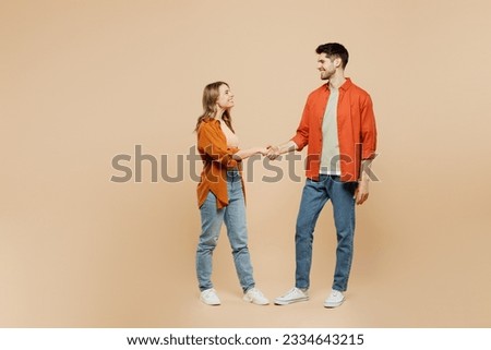 Full body side view young smiling fun couple two friends family man woman wear casual clothes looking to each other shaking hands together isolated on pastel plain light beige color background studio