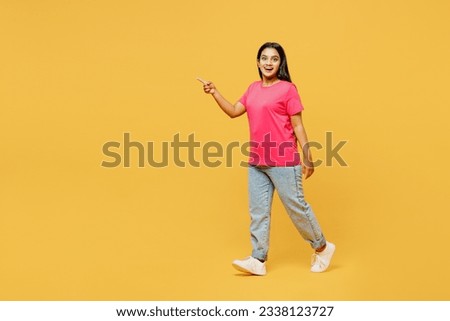 Full body side view young smiling cheerful happy Indian woman wear pink t-shirt casual clothes walking goign point finger aside isolated on plain yellow background studio portrait. Lifestyle concept