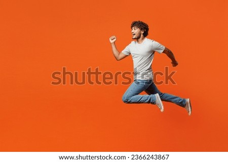 Full body side view young overjoyed excited fun cool smiling happy Indian man wears t-shirt casual clothes jump high run fast isolated on orange red color background studio portrait. Lifestyle concept