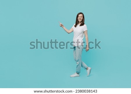 Full body side view young caucasian woman 20s wear white t-shirt walking going strolling point index finger aside on workspace area mock up isolated on plain pastel light blue cyan background studio