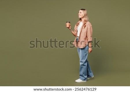 Full body side view young woman she wear red shirt white t-shirt casual clothes hold takeaway delivery craft paper brown cup coffee to go isolated on plain pastel green background. Lifestyle concept