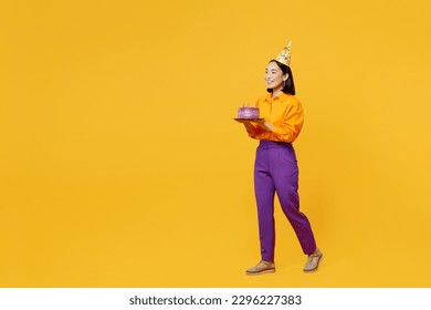 Full body sideways happy smiling fun young woman wears casual clothes hat celebrating hold in hand cake with candles walk go isolated on plain yellow background. Birthday 8 14 holiday party concept