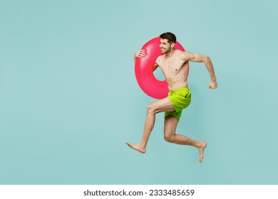 Full body sideways happy young man wearing green shorts swimsuit relax near hotel pool jump high with rubber ring run fast isolated on plain blue background. Summer vacation sea rest sun tan concept - Powered by Shutterstock