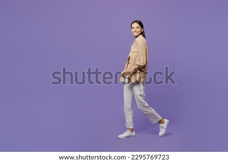 Full body sideways profile smiling happy fun young latin woman wear light shirt casual clothes walk go look camera isolated on plain pastel purple color background studio portrait. Lifestyle concept