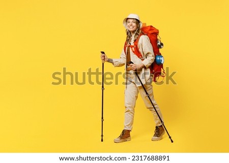 Full body sideways young woman carry bag with stuff mat hold trekking poles isolated on plain yellow background. Tourist leads active lifestyle walk on spare time Hiking trek rest travel trip concept
