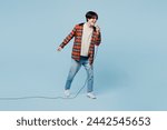 Full body singer expressive young man of Asian ethnicity wears red hoody casual clothes sing song in microphone at karaoke club isolated on plain pastel light blue cyan background. Lifestyle concept