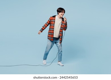 Full body singer expressive young man of Asian ethnicity wears red hoody casual clothes sing song in microphone at karaoke club isolated on plain pastel light blue cyan background. Lifestyle concept - Powered by Shutterstock