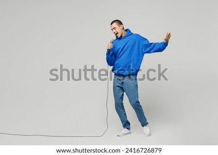 Full body singer young middle eastern man wear blue hoody casual clothes sing song in microphone at karaoke club spread hand isolated on plain solid white background studio portrait. Lifestyle concept