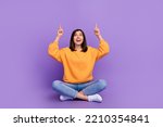 Full body size photo of charming adorable lady sitting crossed legs looking up fingers point mockup useful tips isolated on bright violet color background