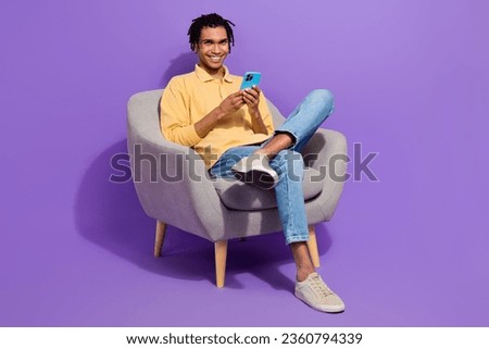 Full body size photo of cheerful student guy sitting soft armchair browsing phone social medias retweet isolated on purple color background