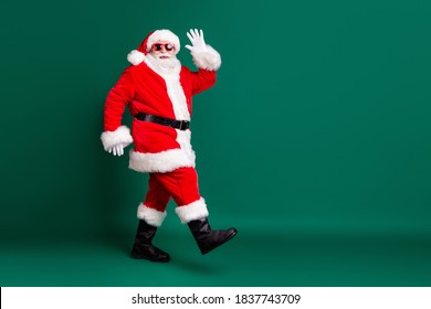 Full body size profile photo of pensioner grandpa walking mall corridors greeting shop customers wear red santa costume coat gloves sunglass headwear isolated green color background - Powered by Shutterstock