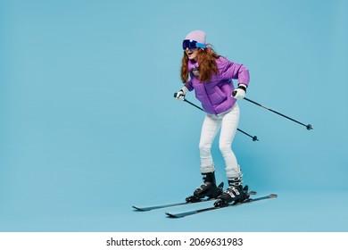 Full body skier smiling happy fun cool woman 20s wearing warm purple padded windbreaker jacket ski goggles mask spend extreme weekend in mountains look camera isolated on plain blue background studio.