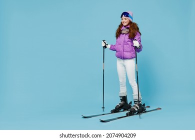 Full body skier smiling happy fun cool woman 20s wearing warm purple padded windbreaker jacket ski goggles mask spend extreme weekend in mountains look aside isolated on plain blue background studio.