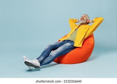 Full Body Sleeping Elderly Gray-haired Mustache Bearded Man 50s In Yellow Shirt Sit In Bag Chair Hold Hands Behind Neck Isolated On Plain Pastel Light Blue Background Studio. People Lifestyle Concept