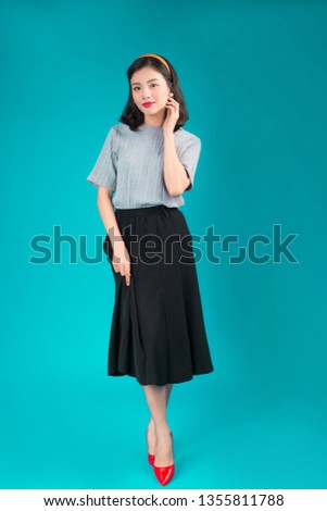Full body of smiling asian woman dressed in pin-up style dress over blue.