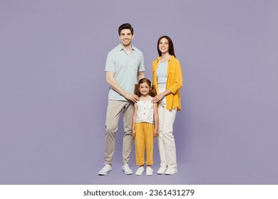 Full body smiling cheerful young parents mom dad with child kid daughter girl 6 years old wear blue yellow casual clothes looking camera posing isolated on plain purple background. Family day concept - Powered by Shutterstock