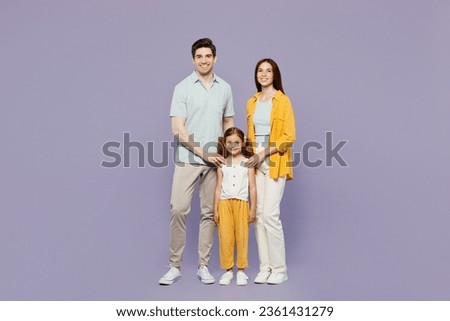 Full body smiling cheerful young parents mom dad with child kid daughter girl 6 years old wear blue yellow casual clothes looking camera posing isolated on plain purple background. Family day concept
