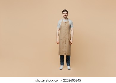 Full body smiling fun young man barista barman employee wear brown apron work in coffee shop look camera isolated on plain pastel light beige background studio portrait Small business startup concept