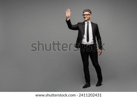 Full body smiling happy adult successful employee business man corporate lawyer wear classic formal black suit shirt tie work in office waving hand isolated on plain grey background studio portrait