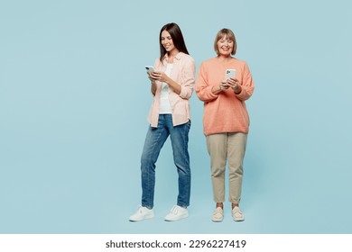 Full body smiling happy cheerful elder parent mom with young adult daughter two women together wear casual clothes hold in hand mobile cell phone isolated on plain blue background. Family day concept - Shutterstock ID 2296227419