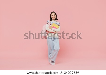 Full body smiling happy cheerful teen student girl of Asian ethnicity wear sweater hold backpack book look camera isolated on pastel plain light pink background Education in university college concept