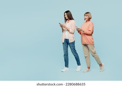 Full body smiling happy elder parent mom with young adult daughter two women together wear casual clothes hold in hand mobile cell phone walk go isolated on plain blue background. Family day concept - Powered by Shutterstock