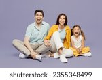 Full body smiling happy fun laughing young happy parents mom dad with child kid daughter girl 6 years old wear blue yellow casual clothes sit isolated on plain purple background. Family day concept